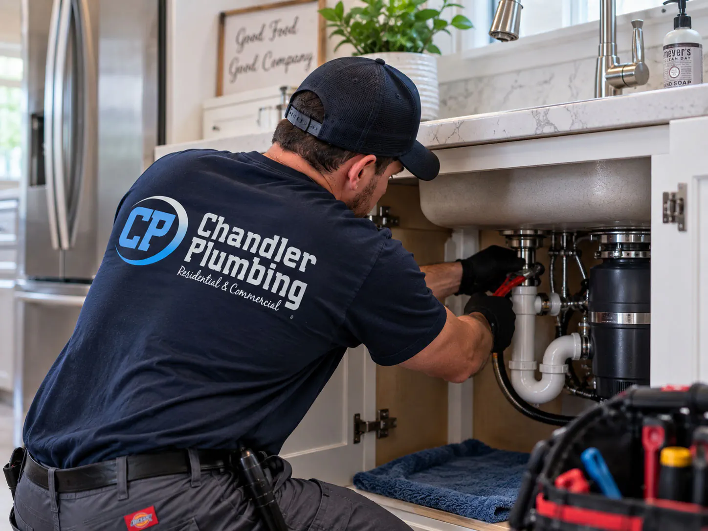 Chandler Plumbing technician working on plumbing beneath a kitchen sink